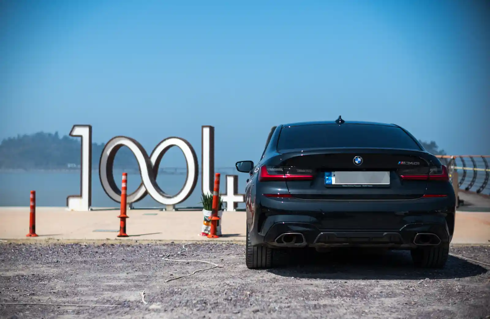신안 자은도 1004 무한의 다리 앞에 주차된 BMW M340i 리어 뷰, 맑은 하늘과 바다를 배경으로