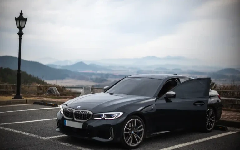 BMW M340i 실사진 — 안개 낀 산을 배경으로 주차된 다크 그레이 M340i 프론트 3/4 앵글
