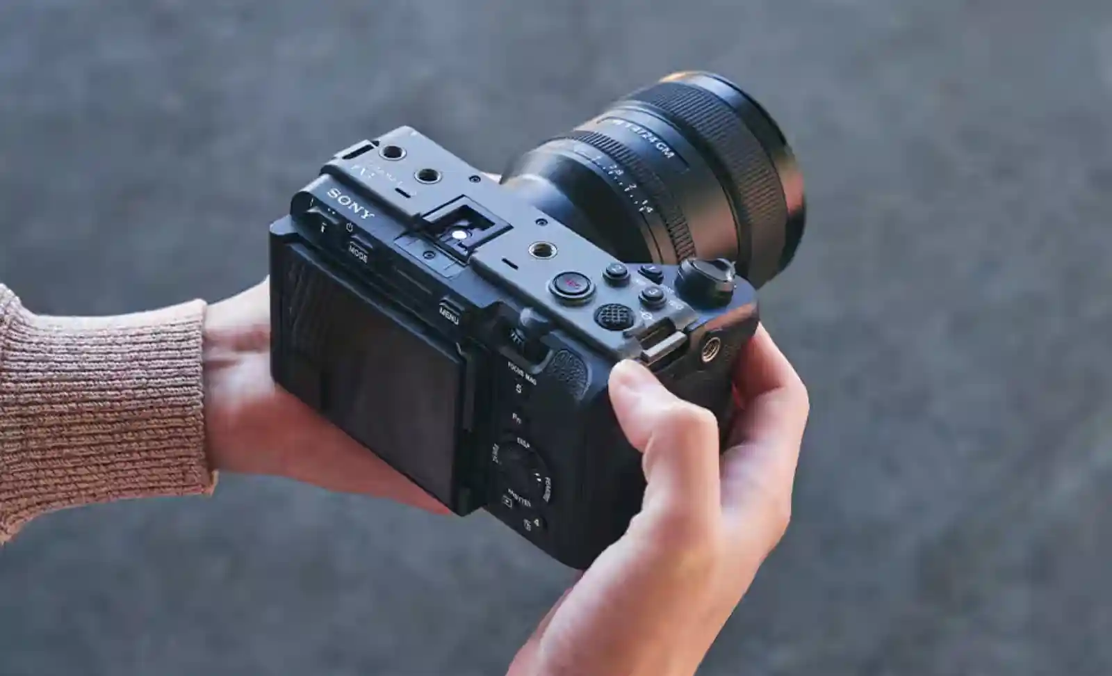 두 손으로 Sony FX3 시네마 라인 미러리스 카메라를 잡고 있는 모습. 틸트 액정이 펼쳐져 있으며 G Master 렌즈가 장착되어 있습니다.
