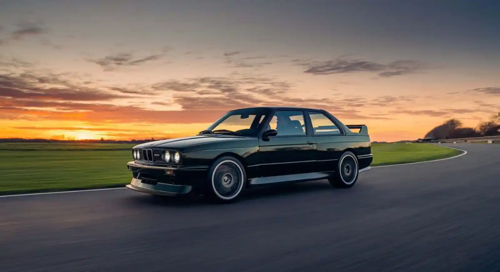 BMW M3 E30 블랙, 서킷 일몰 배경 측면 주행 컷