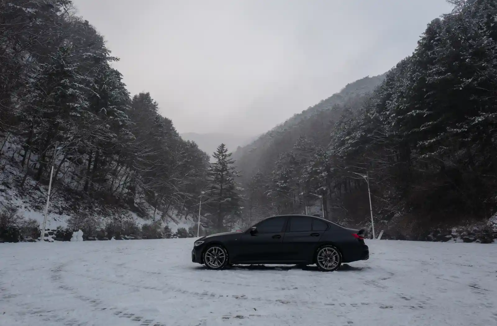 눈 덮인 산악 도로에 정차한 검정 BMW M340i 측면 — 한국 겨울 저온 환경에서의 전기차 배터리 주행거리 비교