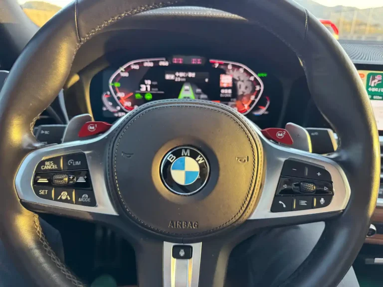 BMW M340i 운전석에서 바라본 스티어링 휠과 디지털 계기판 모습. M1·M2 버튼이 적용된 BMW M 퍼포먼스 모델의 실내 디자인을 보여준다.