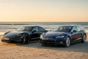 해질녘 바닷가를 배경으로 모래사장 위에 나란히 서 있는 검은색 포르쉐 타이칸과 짙은 파란색의 테슬라 모델 S