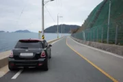 욕지도 해안일주도로 위에 세워진 검정 미니쿠퍼, 왼쪽으로 한려수도 바다와 섬들이 펼쳐지는 드라이브 코스 전경